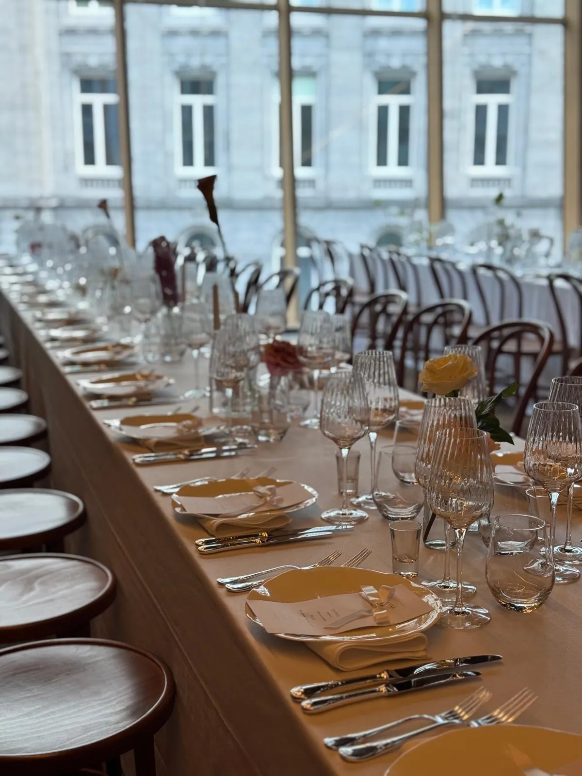 De longues tables dressées pour un grand événement, devant une grande verrière