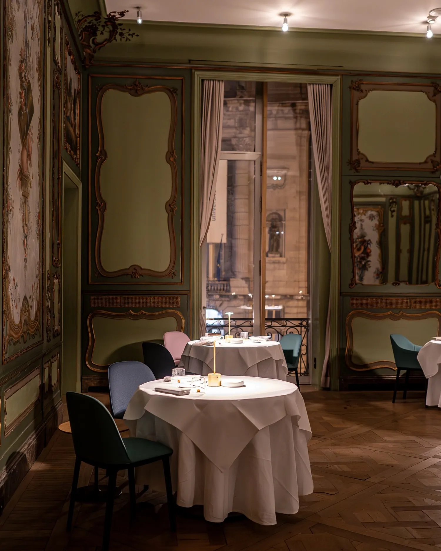 La salle du restaurant Baci : tables dressées, boiseries peintes et fenêtres sur la place